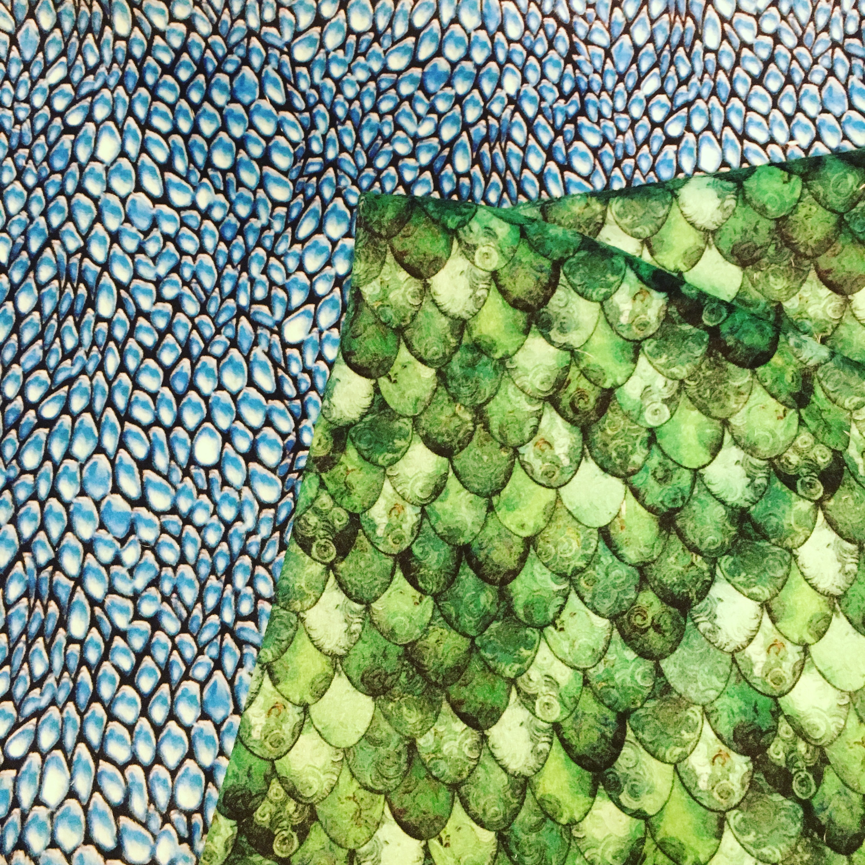 Image of two pieces of fabric, one light blue dragon scale print and one green mermaid scale print.